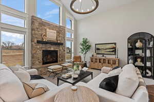 Living room with a stone fireplace, high vaulted ceiling, and a chandelier