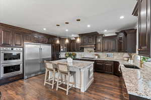 Kitchen featuring dark brown cabinetry, sink, a center island, hanging light fixtures, and stainless steel appliances