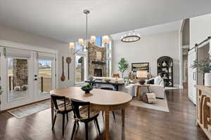 Dining area featuring an inviting chandelier, dark hardwood / wood-style floors, a stone fireplace, and a barn door