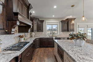 Kitchen featuring appliances with stainless steel finishes, dark hardwood / wood-style flooring, hanging light fixtures, light stone countertops, and dark brown cabinets