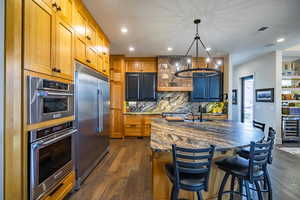 Kitchen featuring a kitchen breakfast bar, stainless steel appliances, a center island with sink, decorative light fixtures, and beverage cooler