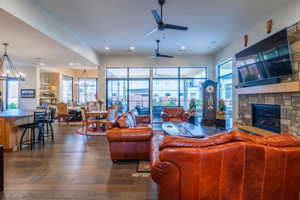 Living room featuring a stone fireplace, dark wood-type flooring, a healthy amount of sunlight, and ceiling fan with notable chandelier