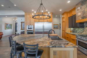 Kitchen featuring sink, an inviting chandelier, high end appliances, a center island with sink, and decorative light fixtures