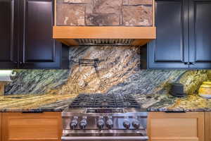 Kitchen with dark stone countertops, backsplash, custom exhaust hood, and gas stove