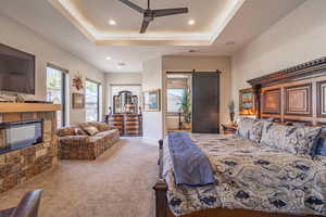 Bedroom featuring light colored carpet, a barn door, a raised ceiling, and a stone fireplace