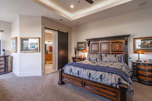 Bedroom featuring light colored carpet, a barn door, a raised ceiling, and ensuite bath