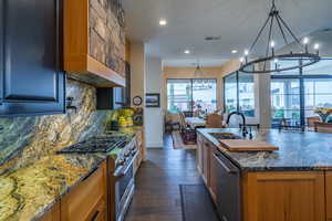 Kitchen with dark stone countertops, appliances with stainless steel finishes, an island with sink, and a notable chandelier