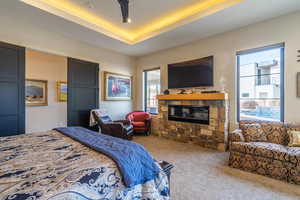 Bedroom featuring light colored carpet, a stone fireplace, and a raised ceiling