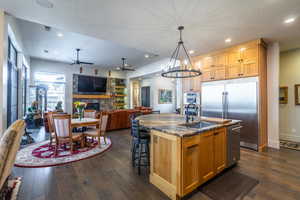 Kitchen with appliances with stainless steel finishes, sink, dark stone countertops, hanging light fixtures, and a kitchen island with sink