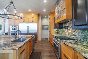 Kitchen with sink, dark stone countertops, hanging light fixtures, high quality appliances, and decorative backsplash