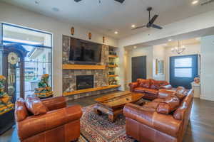 Living room with a fireplace, ceiling fan with notable chandelier, dark wood-type flooring, and a healthy amount of sunlight