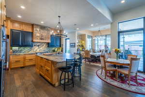 Kitchen featuring pendant lighting, an island with sink, a breakfast bar area, light stone counters, and an inviting chandelier