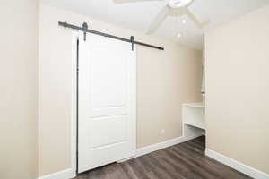 Unfurnished bedroom with ceiling fan, dark hardwood / wood-style floors, a barn door, and a textured ceiling