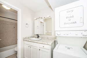 Full bathroom with stacked washer and clothes dryer, toilet, vanity, tiled shower / bath combo, and tile patterned flooring