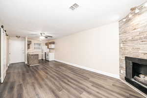 Unfurnished living room featuring ceiling fan, a barn door, dark hardwood / wood-style floors, and a fireplace