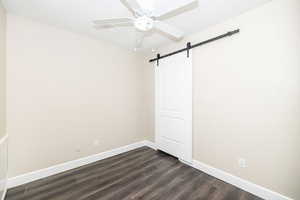 Empty room with dark hardwood / wood-style floors, ceiling fan, and a barn door