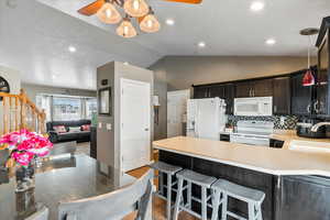 Kitchen featuring sink, vaulted ceiling, kitchen peninsula, pendant lighting, and white appliances