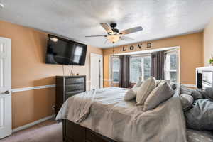 Carpeted bedroom with ceiling fan and a textured ceiling