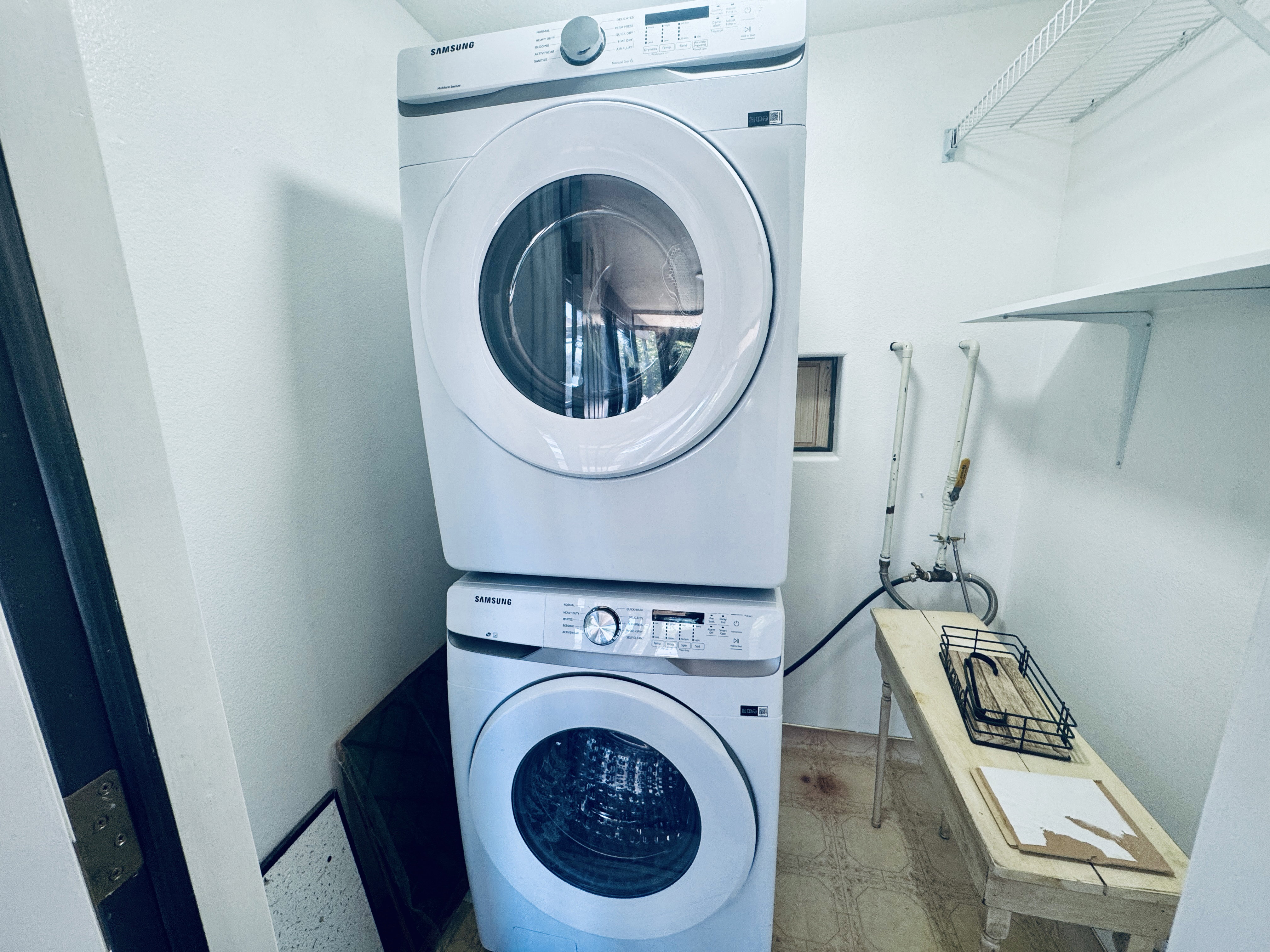 Dedicated laundry area with stackable washer and dryer appliances, wall-mounted shelving, and a small utility window