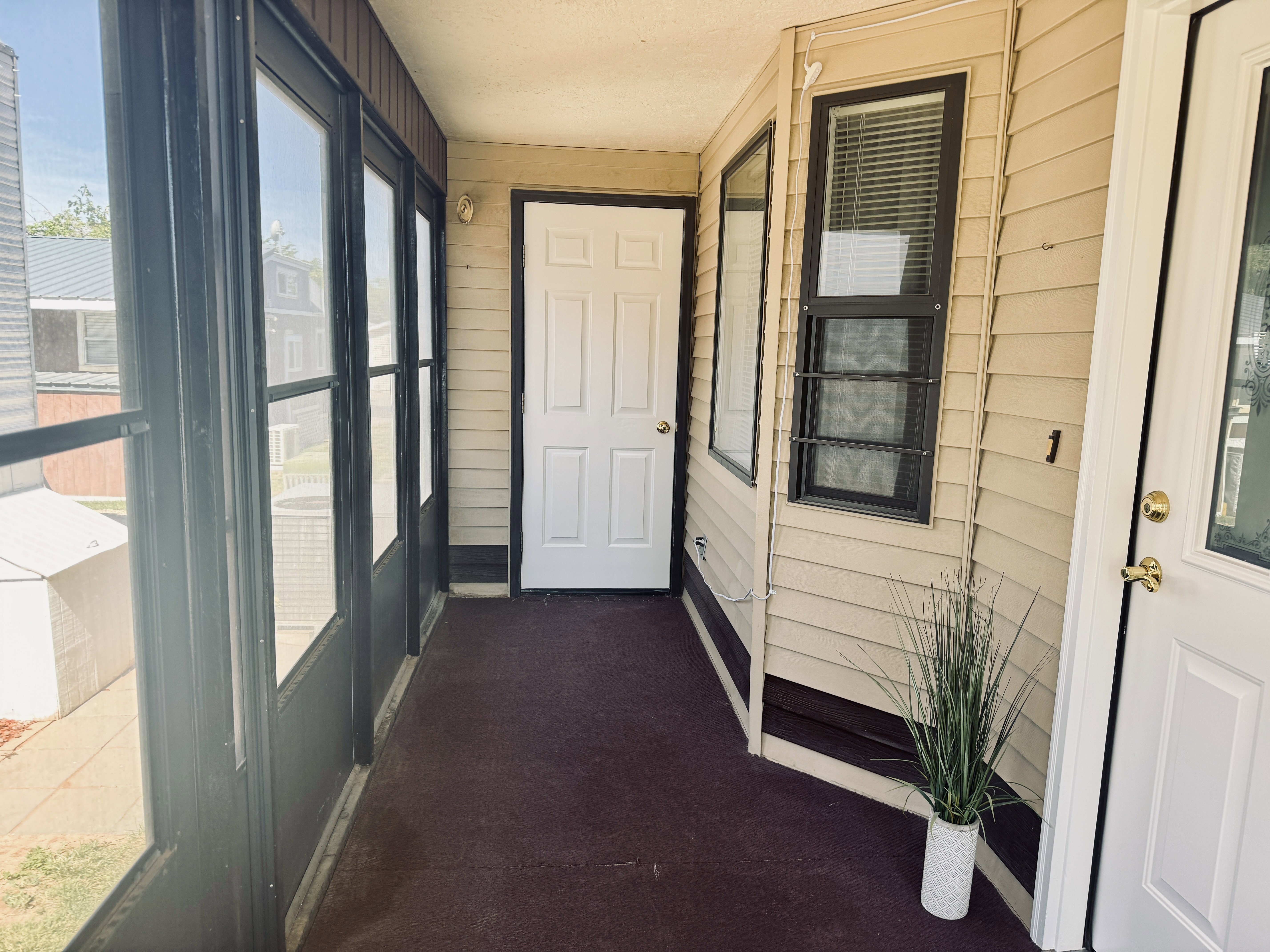 Enclosed screened porch with dark-framed panels and a red-toned carpeted floor