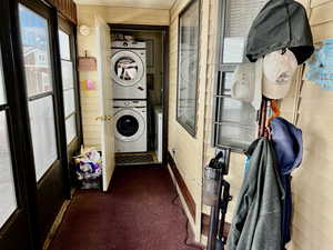 Laundry area featuring stacked washer / drying machine, dark carpet, and wooden walls