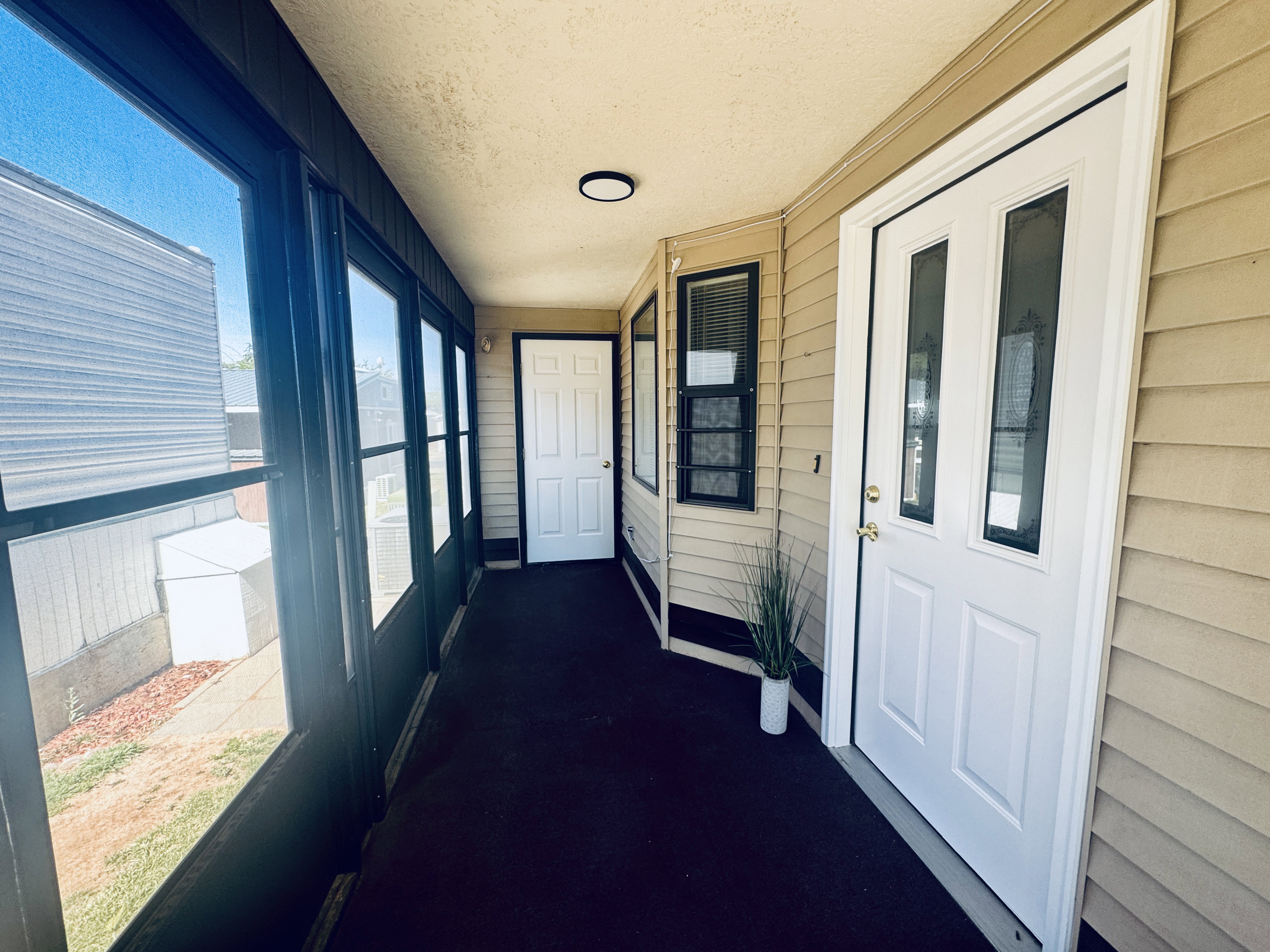 Enclosed porch featuring a full wall of windows, textured exterior siding, and a white panel door with decorative glass inserts