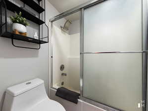 Bathroom with bath / shower combo with glass door and toilet