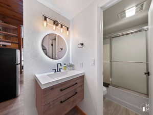 Full bathroom with vanity, wood-type flooring, toilet, and combined bath / shower with glass door