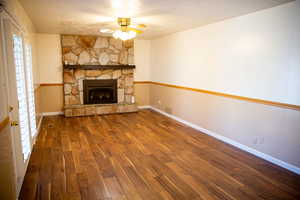 Unfurnished living room with ceiling fan, a stone fireplace, and hardwood / wood-style floors