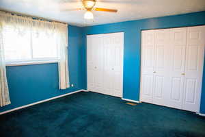 Unfurnished bedroom featuring multiple closets, dark colored carpet, ceiling fan, and a textured ceiling