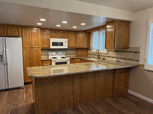 Kitchen with sink, dark hardwood / wood-style flooring, kitchen peninsula, light stone countertops, and white appliances