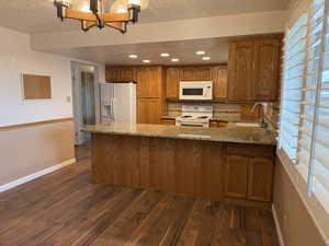 Kitchen featuring sink, white appliances, light stone counters, dark hardwood / wood-style flooring, and kitchen peninsula