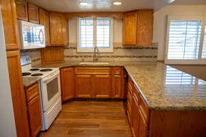 Kitchen featuring hardwood / wood-style floors, tasteful backsplash, sink, light stone counters, and white appliances