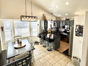 Kitchen with vaulted ceiling, appliances with stainless steel finishes, light tile patterned flooring, decorative light fixtures, and plenty of natural light