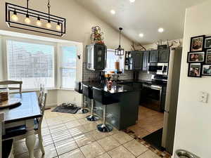 Kitchen with pendant lighting, stainless steel appliances, light tile patterned flooring, and vaulted ceiling