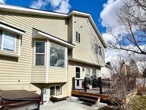 Back of property with a hot tub, a deck, a patio area, and a lawn