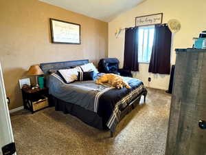 Carpeted bedroom with vaulted ceiling, ceiling fan, and a textured ceiling