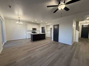 Kitchen with hanging light fixtures, hardwood / wood-style floors, stainless steel appliances, white cabinets, and a center island with sink