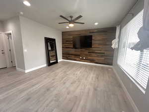 Unfurnished living room featuring ceiling fan, wooden walls, and light hardwood / wood-style floors