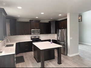 Kitchen with sink, appliances with stainless steel finishes, light hardwood / wood-style floors, a kitchen island, and decorative backsplash