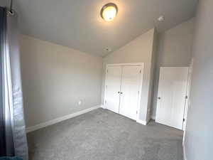 Unfurnished bedroom with vaulted ceiling, a closet, and dark colored carpet