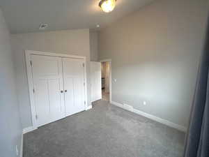 Unfurnished bedroom with dark carpet, high vaulted ceiling, and a closet