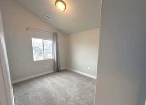 Spare room featuring carpet floors and vaulted ceiling