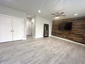 Unfurnished living room with light hardwood / wood-style flooring, ceiling fan, and wood walls