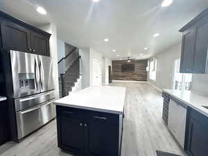 Kitchen featuring appliances with stainless steel finishes, a center island, light hardwood / wood-style floors, and wood walls