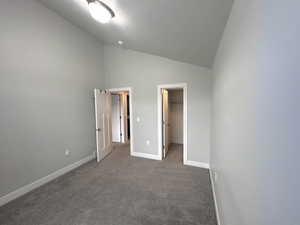 Unfurnished bedroom featuring dark carpet, a walk in closet, high vaulted ceiling, and a closet