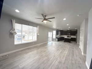 Living room with a textured ceiling, light hardwood / wood-style floors, and ceiling fan