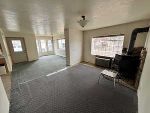 Interior space with a textured ceiling, a wood stove, radiator, carpet, and a baseboard heating unit