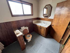 Bathroom featuring vanity, wooden walls, and toilet