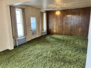 Carpeted spare room with radiator and wood walls